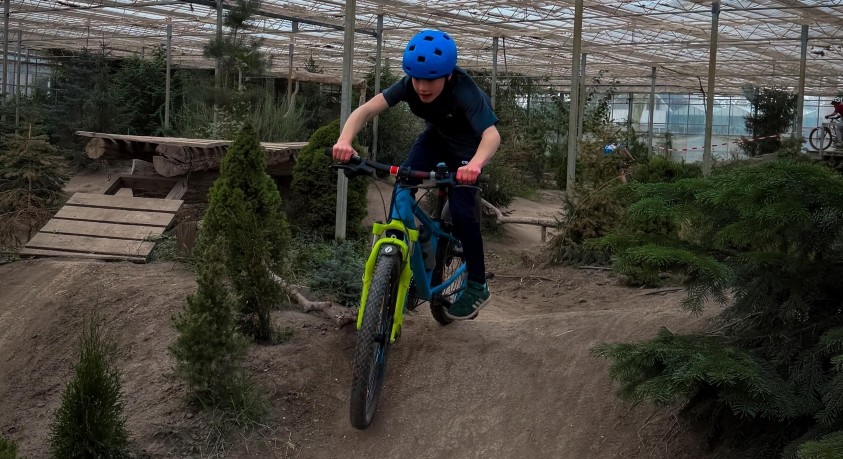 Kind op mountainbike over een indoor mountainbike parcours, omringt door bomen en struiken